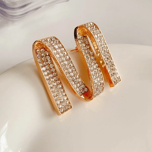 Detailed close-up of golden letter M brooch with sparkling rhinestones on ceramic base
