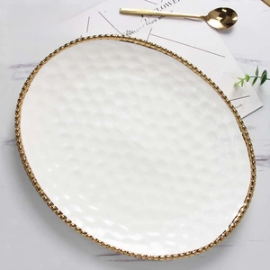 Close-up of white oval ceramic plate with golden beaded edge and hammered texture finish