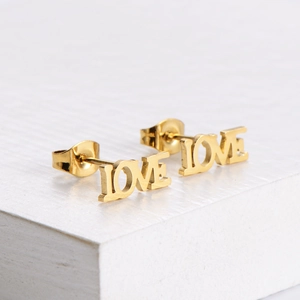 Boucles d'oreilles LOVE en acier doré poli présentées sur un fond blanc texturé