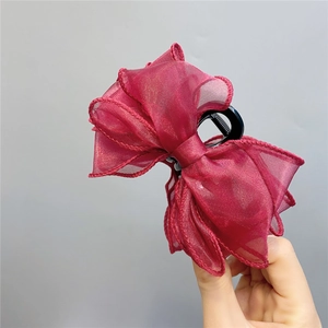 Close-up of red organza bow hair claw clip being held to show size and airy texture