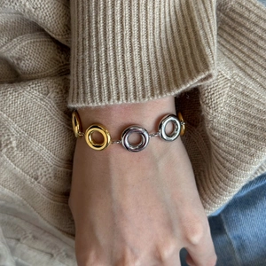 Close-up of minimalist gold and silver interlocking circle bracelet on a knit sleeve