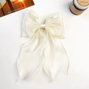 Detail of elegant cream-colored organza bow hair clip with long ribbons on white surface