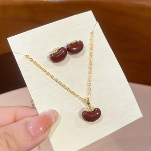 Detail of gold-plated apple pendant necklace and earrings set with red cubic zirconia