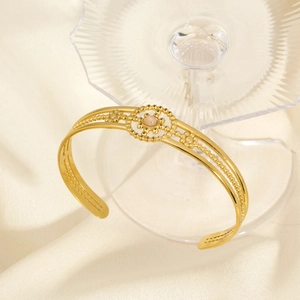 Detail of gold-plated open cuff bracelet with sun flower design and pink gemstone