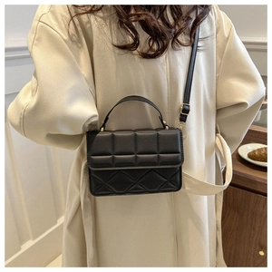 Detail of black quilted crossbody bag featuring a classic textured pattern and top handle