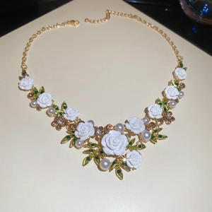 Detailed macro shot of white roses, green enamel leaves, and pearls on a gold necklace