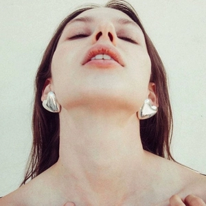 Polished silver heart-shaped stud earrings worn by a model in a minimalist style