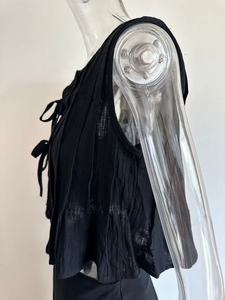 Detail of black pleated cotton sleeveless top featuring delicate front bow tie closures