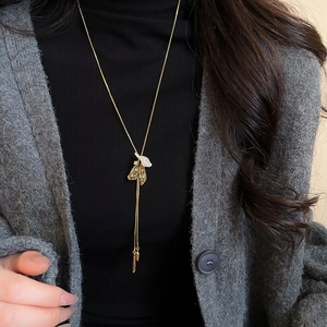 Close-up of golden tassel necklace with shell flower pendant on black knitwear