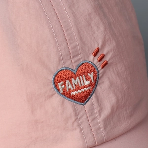 Detail of pink baseball cap with red heart embroidery featuring FAMILY text on creased fabric