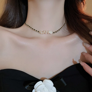 Close-up of golden woven chain necklace with camellia flower and lettered pendant