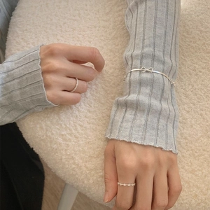 Gros plan d'un bracelet nœud en argent et de deux bagues fines sur fond de peau de mouton