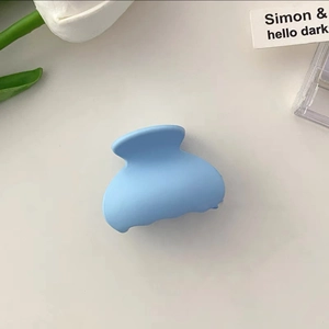Detail of light blue matte hair claw clip on white surface with tulip decoration