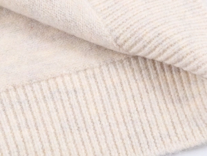Close-up of cream white knit sweater showing ribbed texture and soft wool material