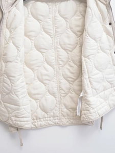 Detailed macro view of wave quilted pattern and fine stitching on the cream vest