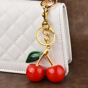 Red resin cherry keychain with golden metal clasp and green leaf on a luxury bag