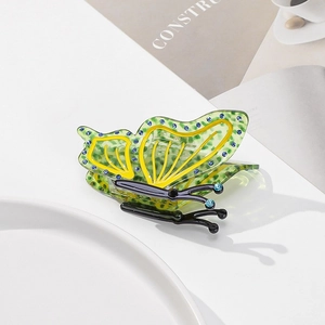 Detail of a green acetate butterfly hair claw clip with blue rhinestones on a white plate