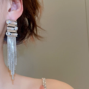Detailed macro view of silver tassel earrings with geometric zircon studs on a model