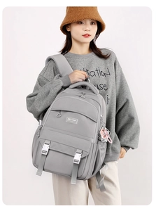 Gray minimalist travel backpack detail showing multiple pockets and decorative white buckles