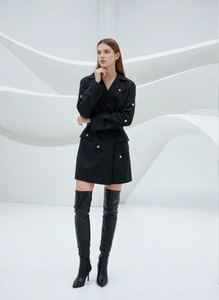 Robe noire chic à double boutonnage avec bottes hautes en cuir dans un décor moderne