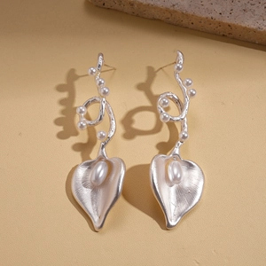 Macro detail of silver leaf vine earrings with pearls on a textured background