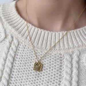 Detail of vintage gold square pendant featuring leaf texture worn on white knit sweater