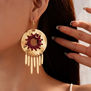 Gros plan sur boucles d'oreilles rondes dorées martelées avec tissage rouge et franges