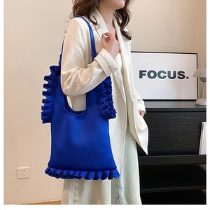 Detail of blue pleated nylon shoulder bag with ruffled edges shown on model