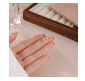 Close-up of elegant gold hollow rose stud earrings held on a finger with a soft focus background