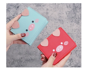 Close-up of cute cartoon pig mini wallets in blue and red PU leather held by hand