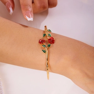 Close-up of a gold rose bangle with red enamel flowers and green leaves on a wrist