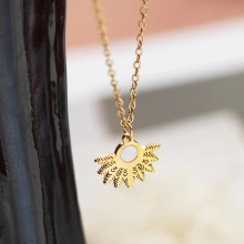 Close-up of golden sunburst pendant with white mother of pearl inlay on a branch