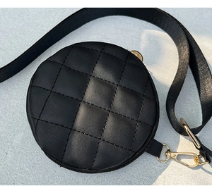 Macro detail of black quilted round bag with golden metal hardware and nylon strap