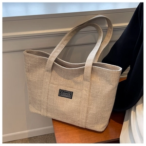 Detail of a large beige canvas tote bag on a wooden bench with fashion label