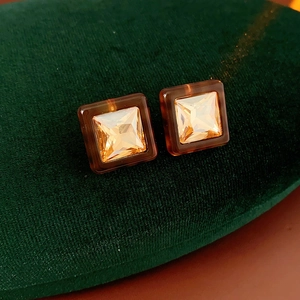 Macro shot of square tortoiseshell earrings with champagne crystal on green velvet