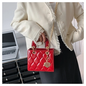 Detailed view of red quilted patent leather handbag with gold chain and heart charm