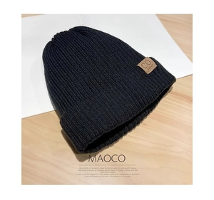 Detail of black cable knit beanie featuring brown leather patch and thick wool texture
