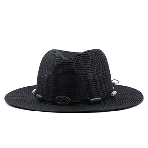 Close-up of black straw fedora hat featuring decorative beads and a metal emblem
