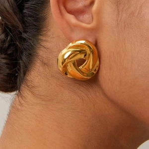 Detail of twisted knot gold earring with high-shine metallic texture worn by a model