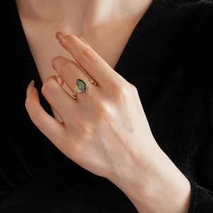 Dettaglio dell'anello dorato con pietra verde oliva taglio marquise al dito