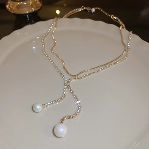 Close-up of gold-layered Y-necklace with rhinestones and pearl pendants on a white plate