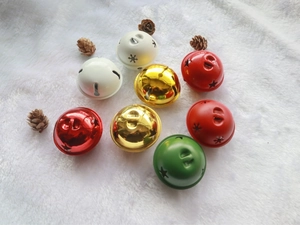 Macro view of 5cm colorful metal bells with star cutouts on a soft white plush background