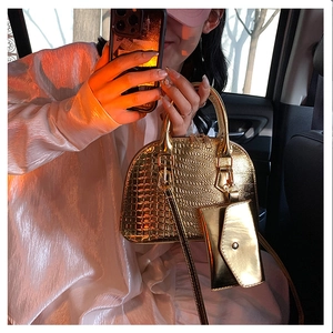 Detail of golden shell bag with crocodile texture and mini charm in car setting