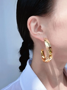 Close-up of model wearing large mirror-polished gold hoop earrings with metallic texture