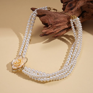 Dettaglio di collana di perle multistrato con ciondolo a fiore dorato su un ramo di legno