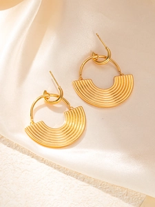 Detailed view of golden geometric earrings with textured fan-shaped pendants on silk fabric