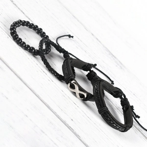 Set di 4 bracciali in pelle nera con ciondolo infinito su sfondo in legno chiaro