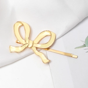 Detail of cream enamel bow hair clip with gold metal frame on a soft fabric base