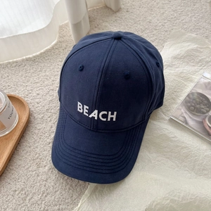 Macro detail of navy blue cotton baseball cap with white BEACH embroidery on the crown