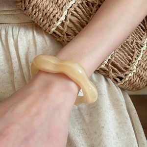 Close-up of irregular wavy cream acrylic bracelet styled with linen clothing and straw bag